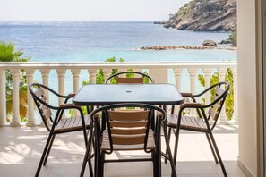 A balcony with a table and chairs, overlooking a coastal landscape with cliffs and the sea. - NEW: Beachfront Blue Bay Beach Ocean 13 (Sint Michiel)