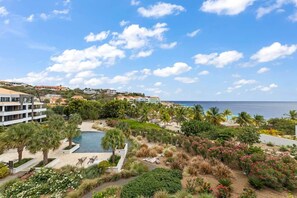 A resort with a swimming pool, palm trees, and a view of the ocean. - NEW: Beachfront Blue Bay Resort The Shore 6 (Sint Michiel)