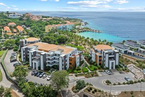 A coastal hotel complex with multiple buildings, parking areas, and a view of the ocean. - NEW: Beachfront Blue Bay Resort The Shore 6 (Sint Michiel)