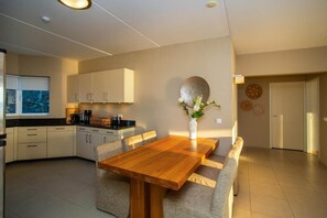 A modern kitchen with a dining area, featuring a wooden table and chairs, a vase with flowers, and a view of the city. - NEW: Beachfront Ocean Suite 5 Blue Bay Beach (Sint Michiel)