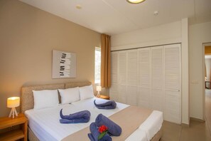 A hotel room with a bed, a nightstand, a lamp, a wall art piece, and a closet. - NEW: Beachfront Ocean Suite 5 Blue Bay Beach (Sint Michiel)