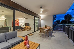 A modern living room with a sofa, dining table, and chairs, a balcony with a railing, and a view of the outdoors. - NEW: Blue Bay Beach Resort The Breeze Oasis (Sint Michiel)