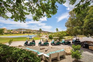 A golf course with a row of golf carts parked near a seating area with a view of the course. - NEW: Blue Bay Beach Resort The Breeze Oasis (Sint Michiel)