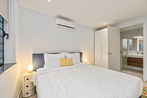 Un dormitorio con cama, lámparas de noche, aire acondicionado, armario y baño con espejo y lavamanos.