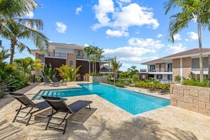 A swimming pool with lounge chairs, surrounded by palm trees and a building with balconies. - NEW: Blue Bay Beach Resort The Breeze Oasis (Sint Michiel)