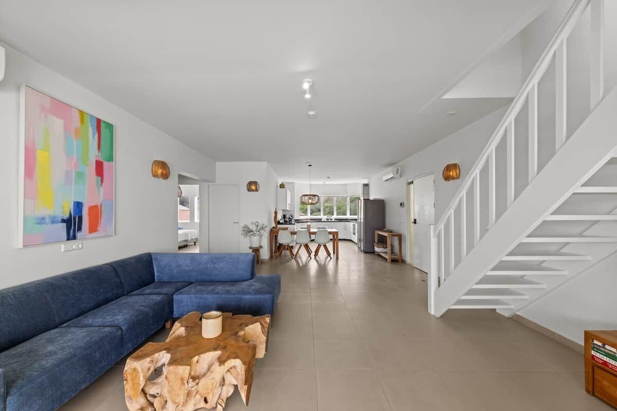 A spacious living area with a blue sectional sofa, a wooden coffee table, and a staircase with white railings.