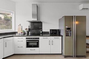 A modern kitchen with white cabinets, a stainless steel range hood, a built-in oven, a microwave, and a large refrigerator. - NEW: Blue Bay Beachfront Penthouse 3BDR (Sint Michiel)