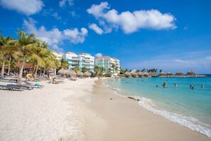 A beach with palm trees, a swimming pool, and a hotel with multiple floors. - NEW: Blue Bay Beachfront Penthouse 3BDR (Sint Michiel)