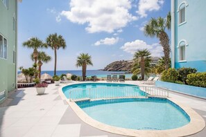 A pool area with a view of the ocean, surrounded by palm trees and lounge chairs. - NEW: Blue Bay Beachfront Penthouse 3BDR (Sint Michiel)