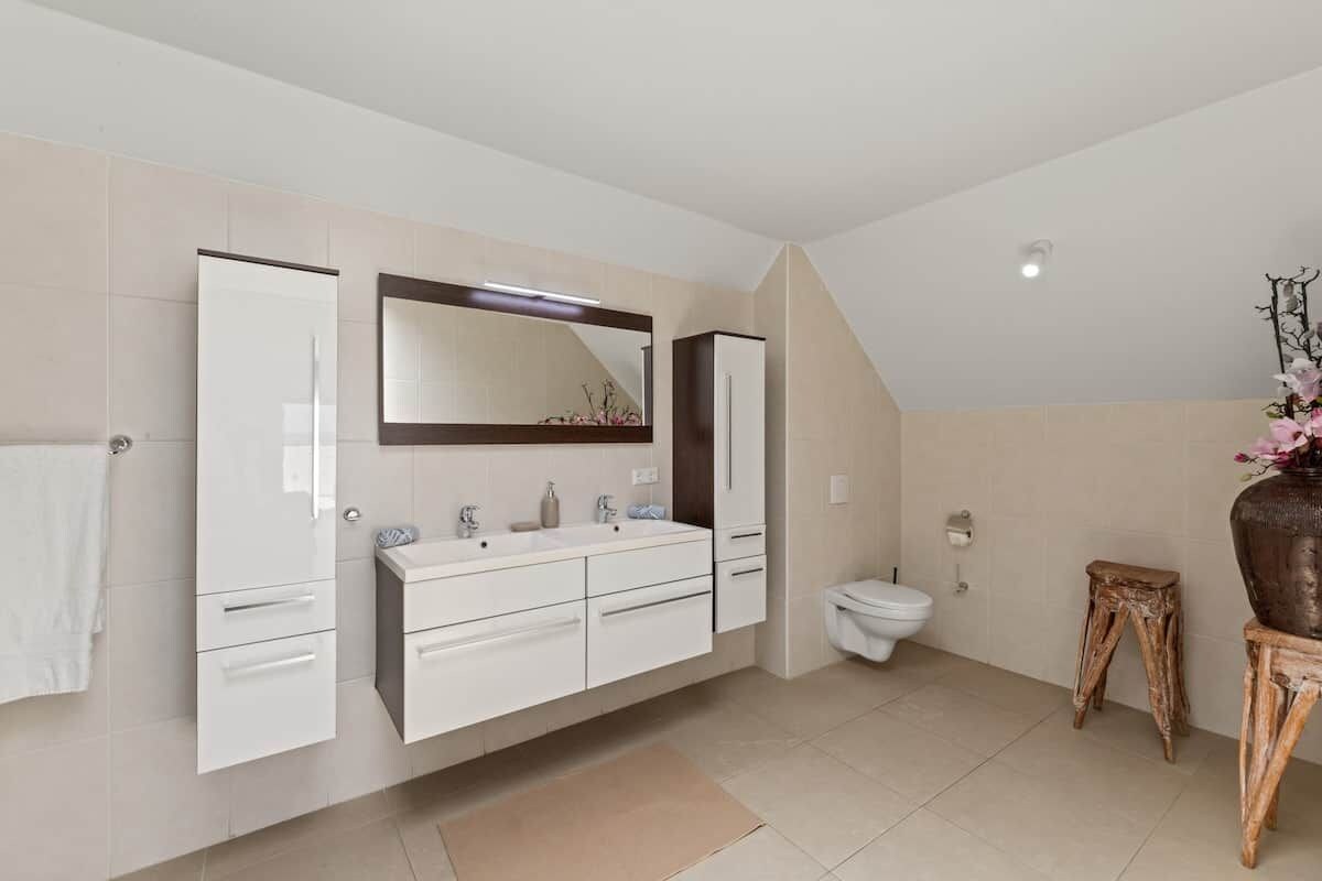 A modern bathroom with a large mirror, a vanity with drawers, a toilet, and a small wooden stool.
