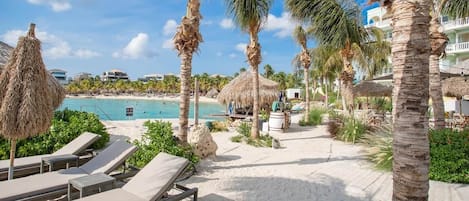 A beachside resort with lounge chairs, palm trees, and a view of the ocean.
