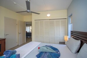 A hotel room with a bed, a ceiling fan, a bedside lamp, and a view of a balcony. - NEW: Blue Bay Beachfront Ocean Suite 23 (Sint Michiel)