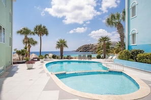 A pool area with a view of the ocean, surrounded by palm trees and lounge chairs. - NEW: Blue Bay Beachfront Ocean Suite 23 (Sint Michiel)