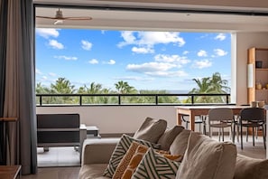 A modern living room with a large window overlooking palm trees and the ocean. - NEW: The Shore 16 Beachfront on Blue Bay Beach (Sint Michiel)