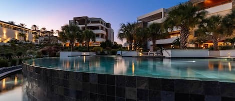 Ein modernes Hotel mit Pool, Palmen und einem Sonnenuntergangshimmel.