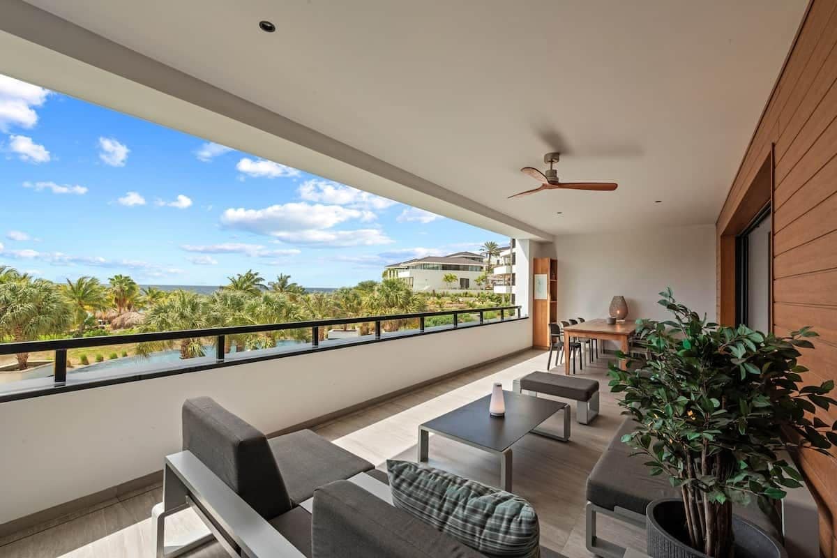 A balcony with a view of a pool and buildings, furnished with sofas and tables.