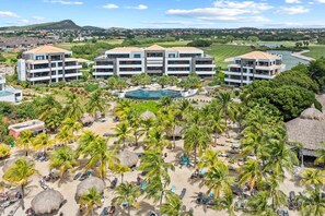 A resort with multiple buildings, a swimming pool, and a beach area with palm trees and sun loungers. - NEW: The Shore 16 Beachfront on Blue Bay Beach (Sint Michiel)