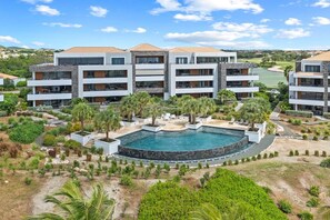 Un hôtel à plusieurs étages doté d’une piscine entourée de verdure, avec un terrain de golf en arrière-plan.