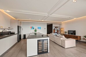 Une cuisine moderne avec un îlot central, un coin repas avec un canapé et un salon équipé d’un téléviseur.