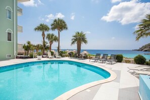 Ein Pool mit Liegestühlen und Palmen, mit Blick auf ein Gewässer.
