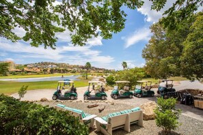 Ein Golfplatz mit mehreren Golfcarts, geparkt in der Nähe einer Sitzgelegenheit mit Bänken.