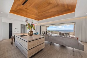A modern kitchen with a central island, a dining area with a view, and a living space with a sofa. - NEW: The Ridge, Penthouse on The Blue Bay Resort (Sint Michiel)