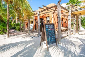 A beachside establishment with a wooden pergola, a chalkboard sign listing services like PADI 5* and IDC Center, and a palm tree in the background. - NEW: Shorefront Suite on the Blue Bay Beach (Sint Michiel)