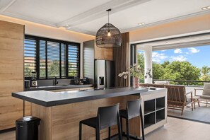 A modern kitchen with a central island, bar stools, and a hanging light fixture. - NEW: Shorefront Suite on the Blue Bay Beach (Sint Michiel)