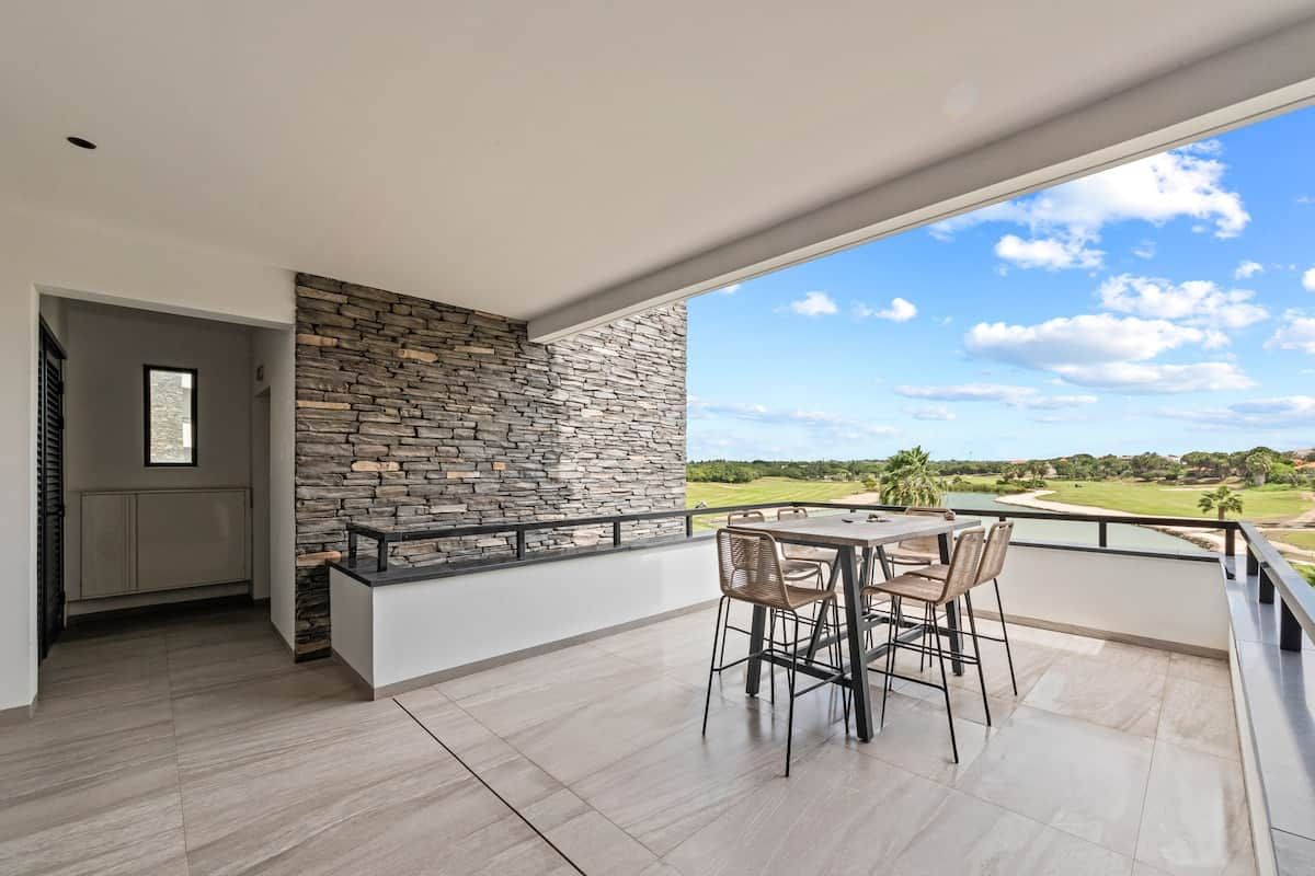 Ein modernes Interieur mit einer Steinwand, einem Balkon mit Blick auf einen Golfplatz und einem Essbereich mit Stühlen und Tisch.