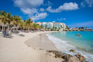 A beach with a row of palm trees, a sandy shore, and a building with balconies overlooking the sea. - NEW: Shorefront Suite on the Blue Bay Beach (Sint Michiel)