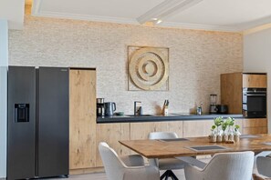 A modern kitchen with a wooden island, stainless steel appliances, and a dining area with a wooden table and chairs. - NEW: The Shore Beachfront Blue Bay Resort 3 BDR (Sint Michiel)