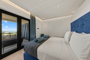 A modern hotel room with a large bed, a view of the ocean, and a balcony with outdoor seating. - NEW: The Shore Beachfront Blue Bay Resort 3 BDR (Sint Michiel)