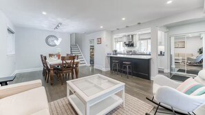 Uma sala de estar moderna com área de jantar, cozinha com balcão e escada.
