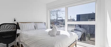 Une chambre avec une grande fenêtre, un lit, un bureau et une chaise.