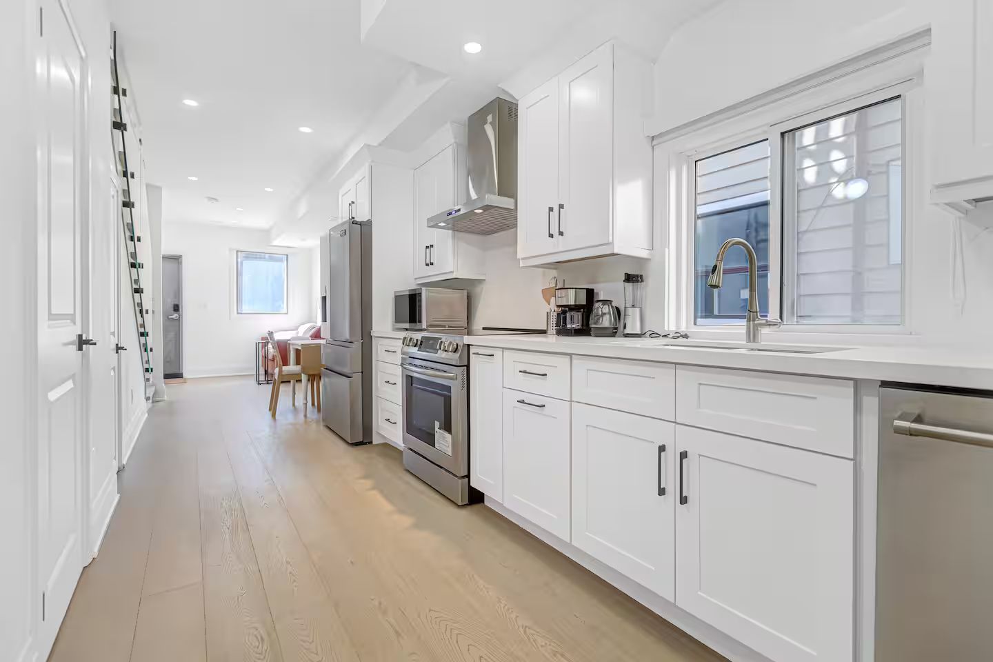 A modern kitchen with white cabinetry, stainless steel appliances, and a window providing natural light.