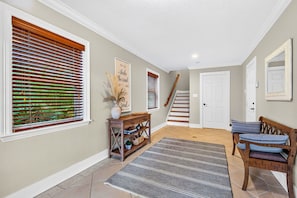 A hallway with a staircase, a console table with decorative items, a bench with cushions, and a patterned rug. - Orange Crush - Private Pool Home Near Beach - By Island Real Estate (Holmes Beach)