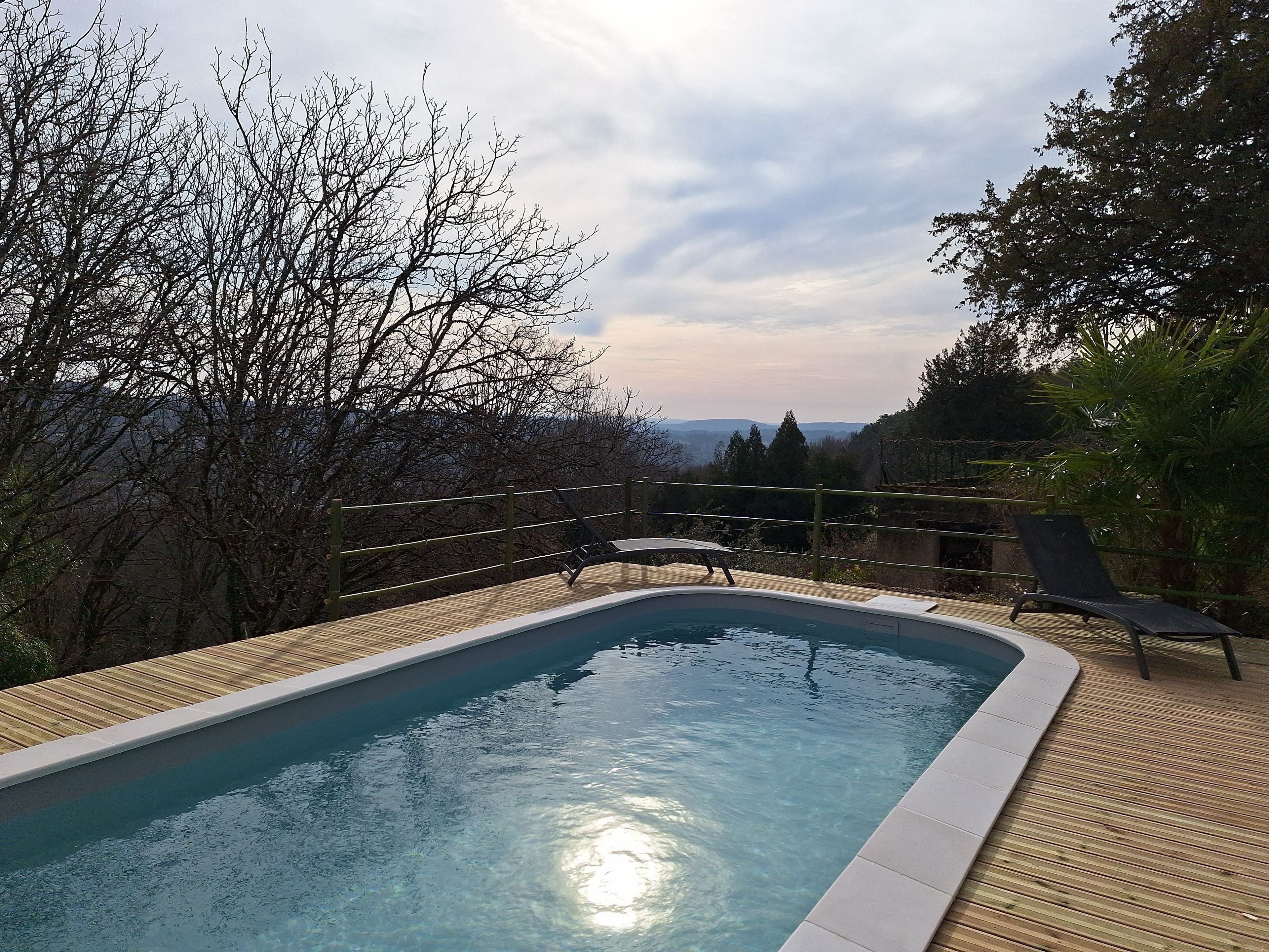 Una piscina con bordo in legno, circondata da alberi e vista su montagne lontane.