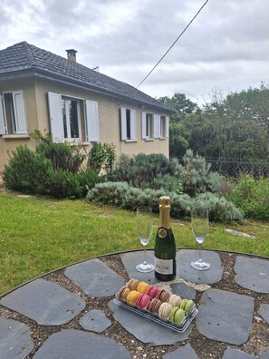 Une table en pierre sur laquelle se trouvent une bouteille de champagne, deux verres et une assiette de macarons, le tout dans un cadre de jardin.