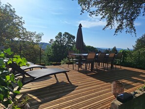 Eine Terrass mit Tisch und Stühlen, umgeben von Grün und mit Blick auf eine schöne Landschaft.
