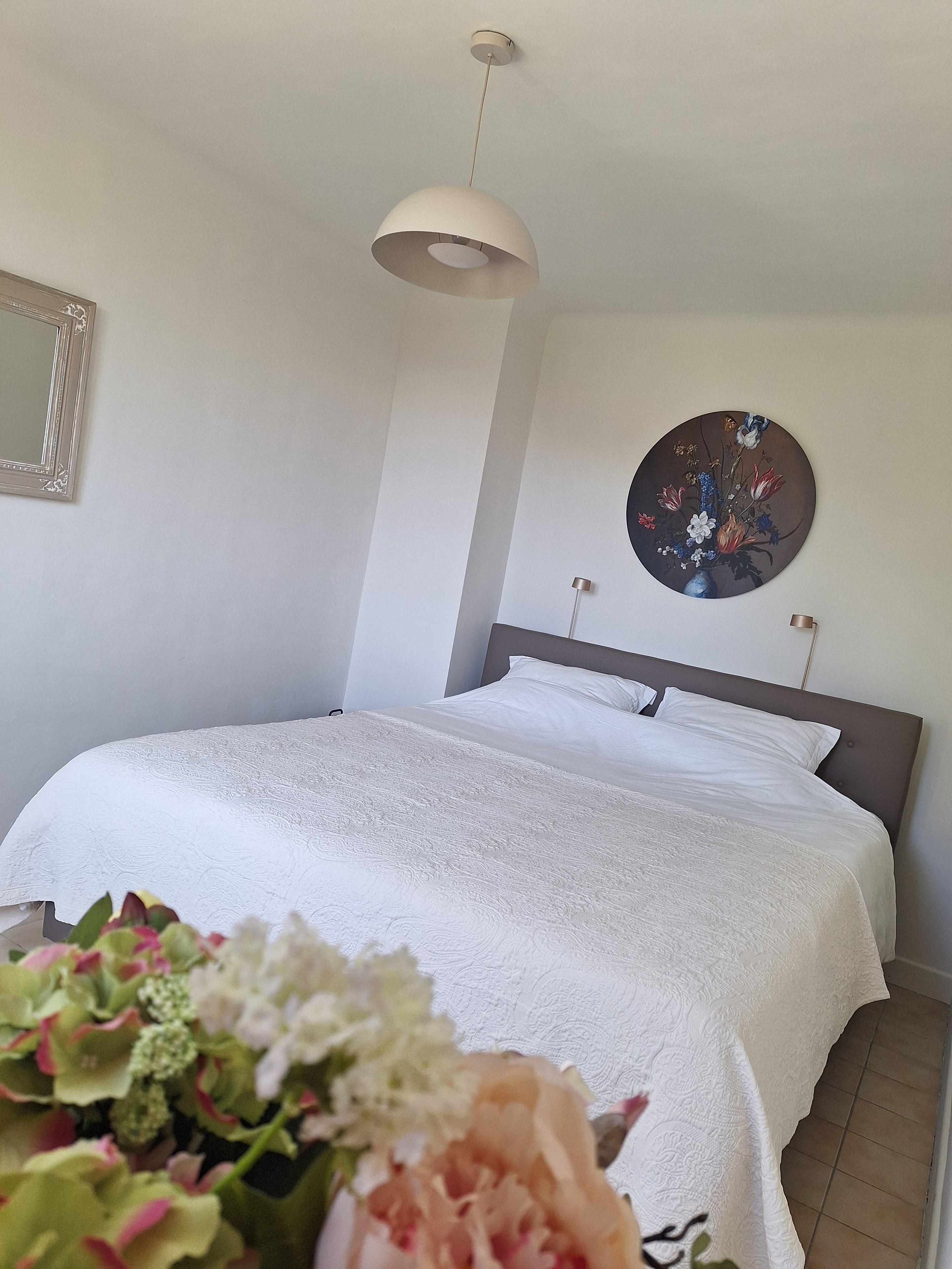 Une chambre à coucher avec un lit, un luminaire suspendu, un tableau accroché au mur et un miroir.