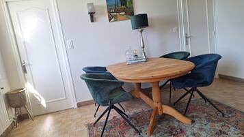 A dining area with a round wooden table, two blue chairs, a patterned rug, and a painting on the wall.