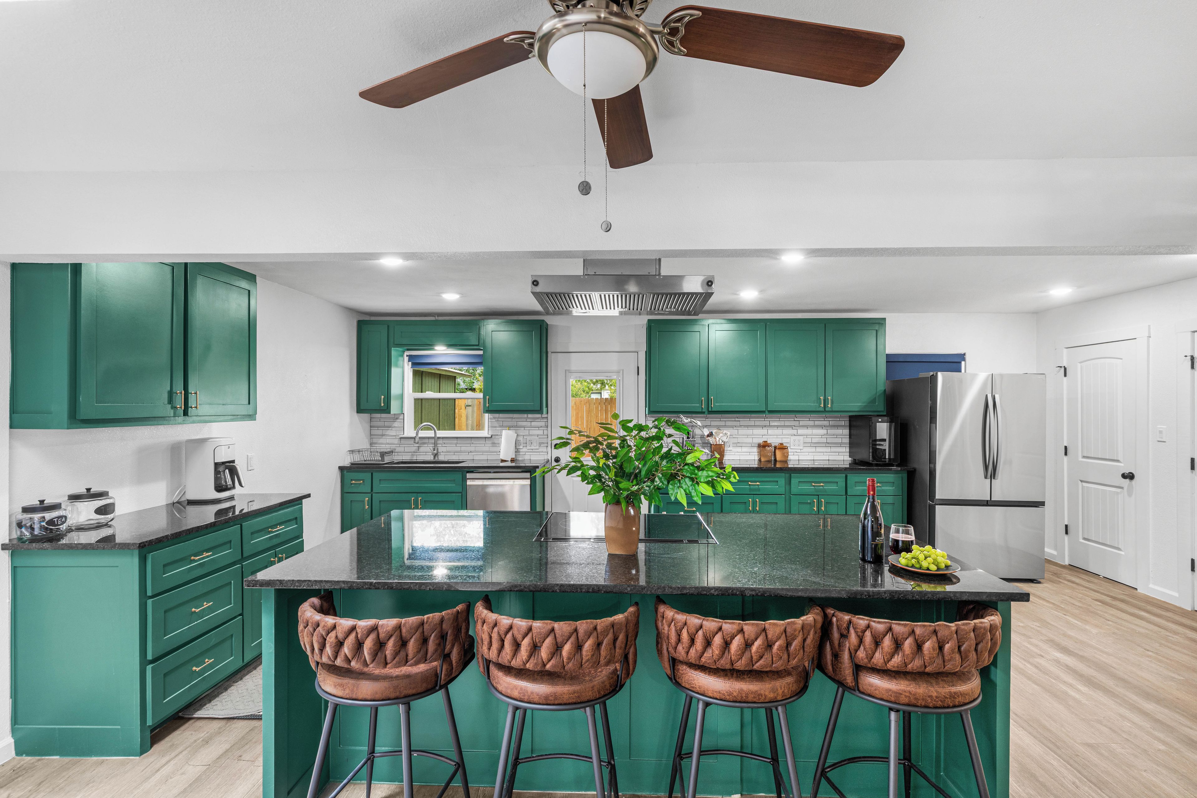 A modern kitchen with green cabinets, a central island, bar stools, and a ceiling fan.