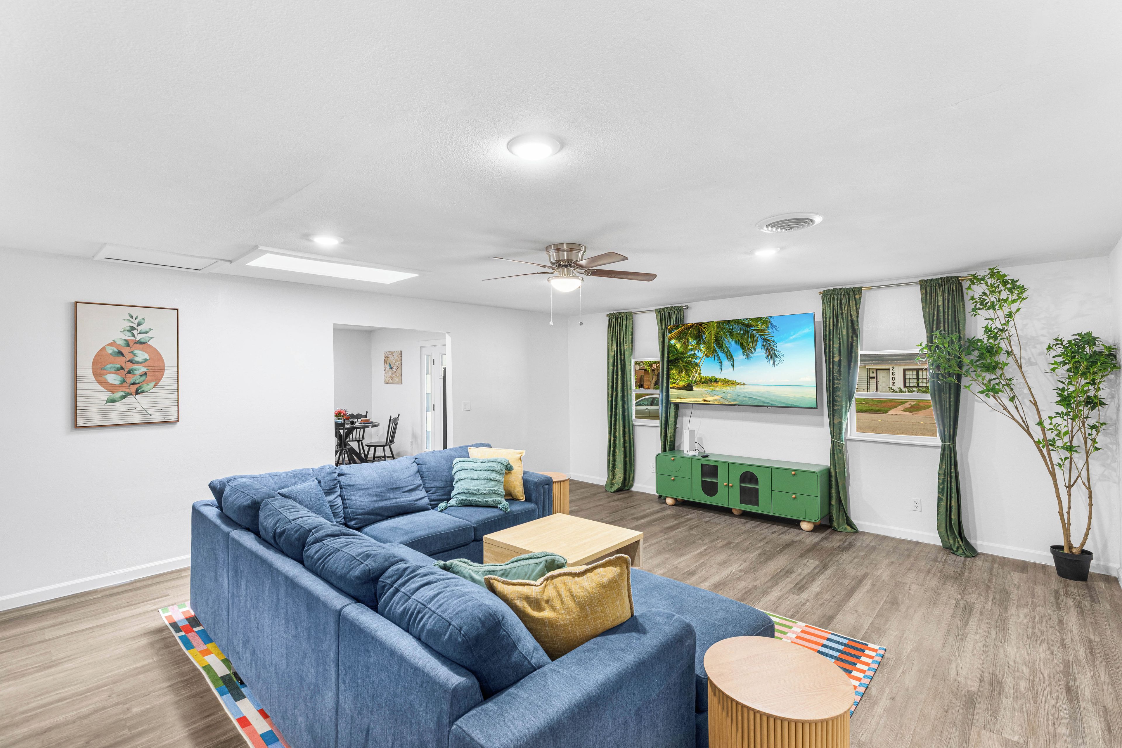 A modern living room with a sectional sofa, a flat-screen TV, and a ceiling fan.