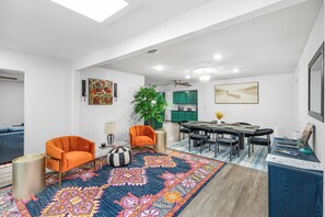 A modern living room with a large rug, two orange armchairs, a dining area with a table and chairs, and a kitchen in the background. - The Big Country Cactus – Spacious 4BR Home Near Dyess AFB, Job Sites & Colleges (Abilene)