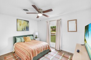 A bedroom with a bed, a ceiling fan, a window with curtains, a painting, and a TV. - The Big Country Cactus – Spacious 4BR Home Near Dyess AFB, Job Sites & Colleges (Abilene)
