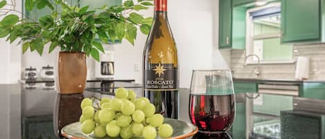 A kitchen counter with a bottle of rosé wine, a glass of red wine, and a plate of green grapes.
