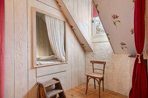 A room with a sloped ceiling, a window with white curtains, a wooden chair, and a small wooden shelf. - BiâO Gîte en Cotentin Holiday Home with Private Terrace, Garden, and Wi-Fi (Bretteville-sur-Ay)