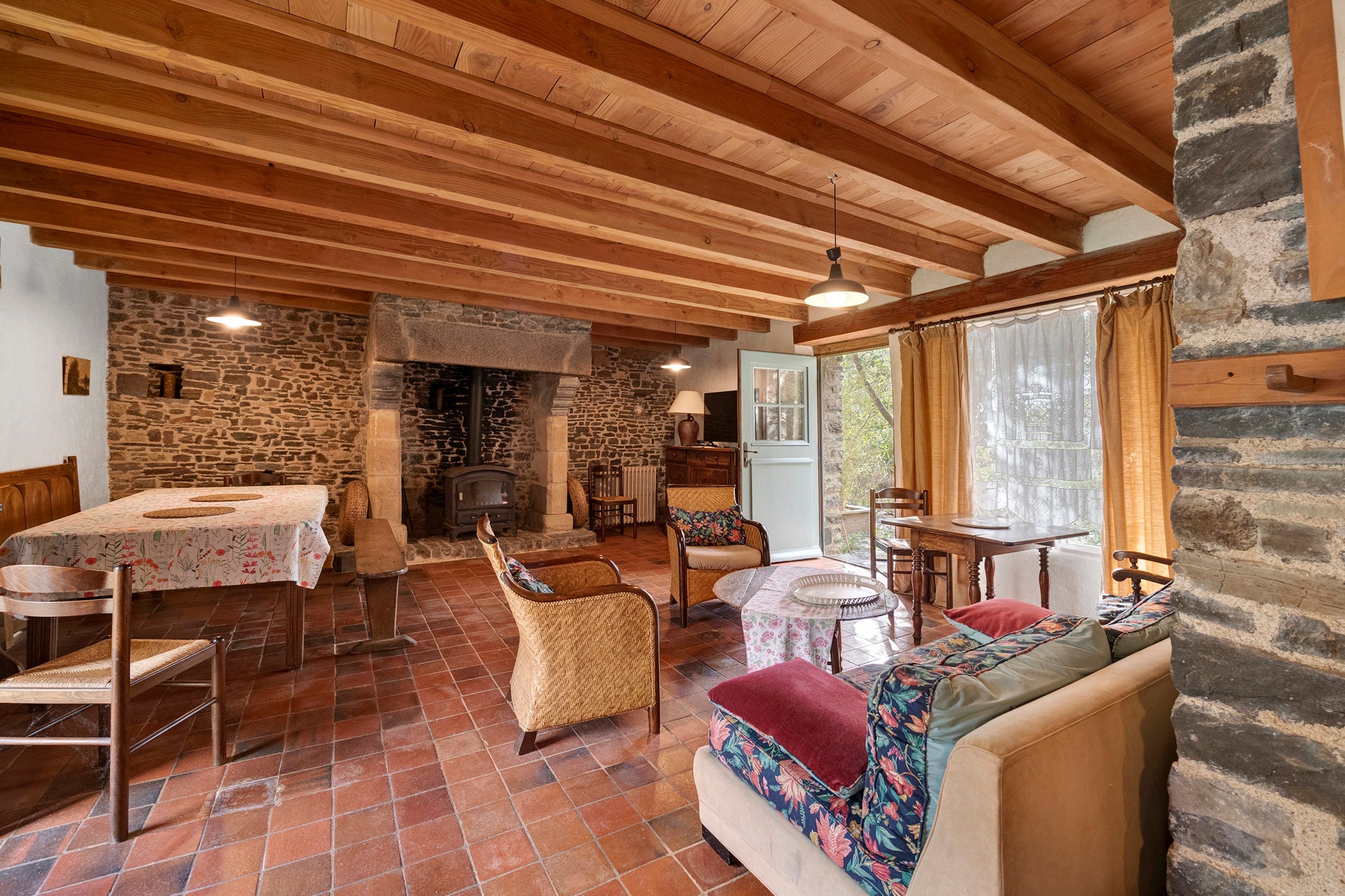 Un intérieur rustique agrémenté d’une cheminée en pierre, de poutres apparentes, d’un coin repas et d’un espace détente offrant une vue agréable.