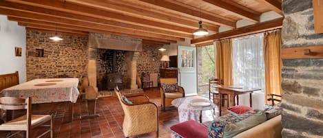 A rustic interior with a stone fireplace, wooden beams, a dining area, and a seating area with a view.