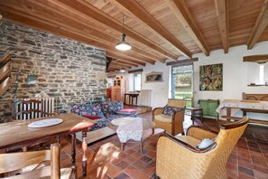 Un interno rustico con parete in pietra, travi in legno, un divano, sedie in vimini e un tavolo da pranzo.